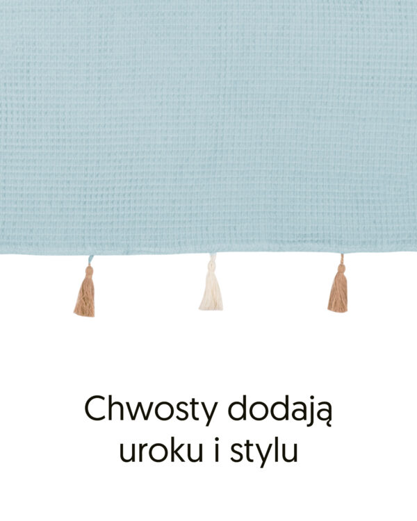 Brzeg poncza z bawełny waflowej w kolorze błękitnym i ozdobne chwosty, z podpisem „Chwosty dodają uroku i stylu”.