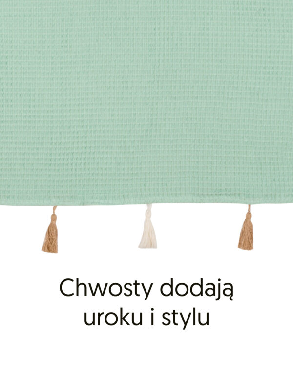 Brzeg poncza z bawełny waflowej w kolorze miętowym i ozdobne chwosty, z podpisem „Chwosty dodają uroku i stylu”.